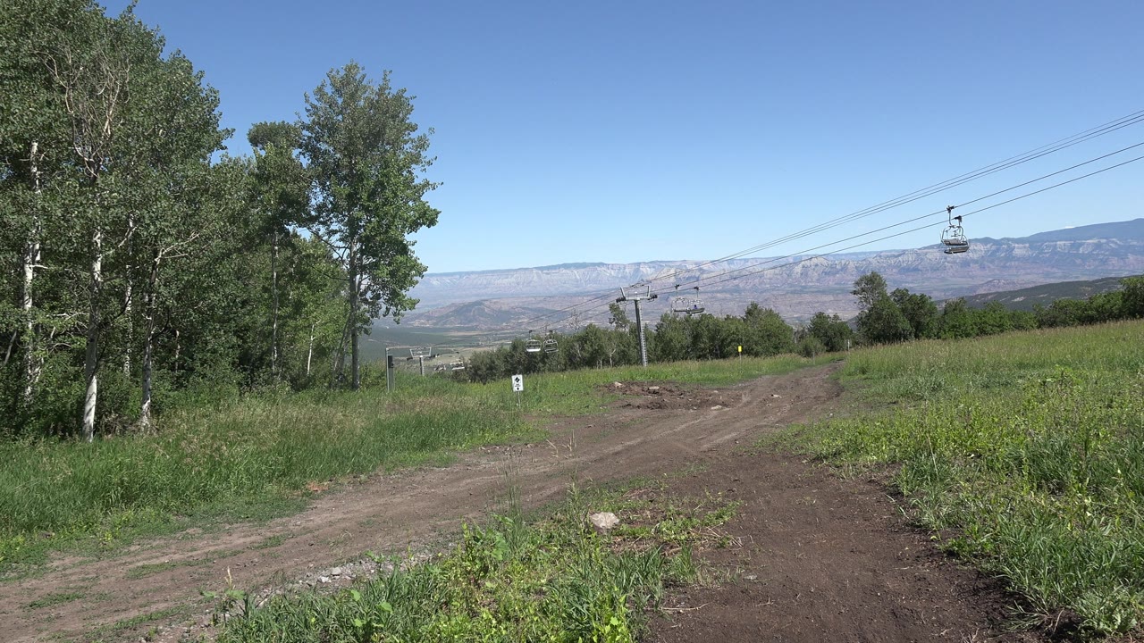 Green hillside trail with cable cars and distant mountains.