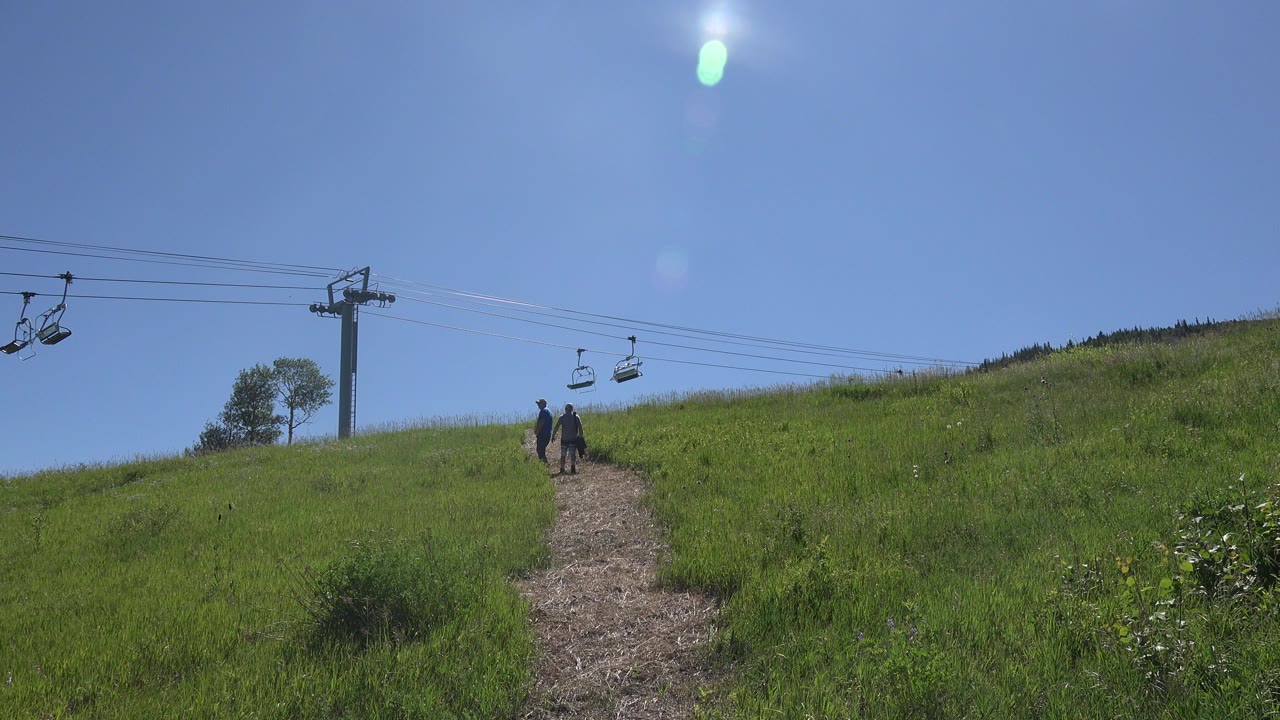 Two people walk up a grassy hillside path beneath chair lift cables.