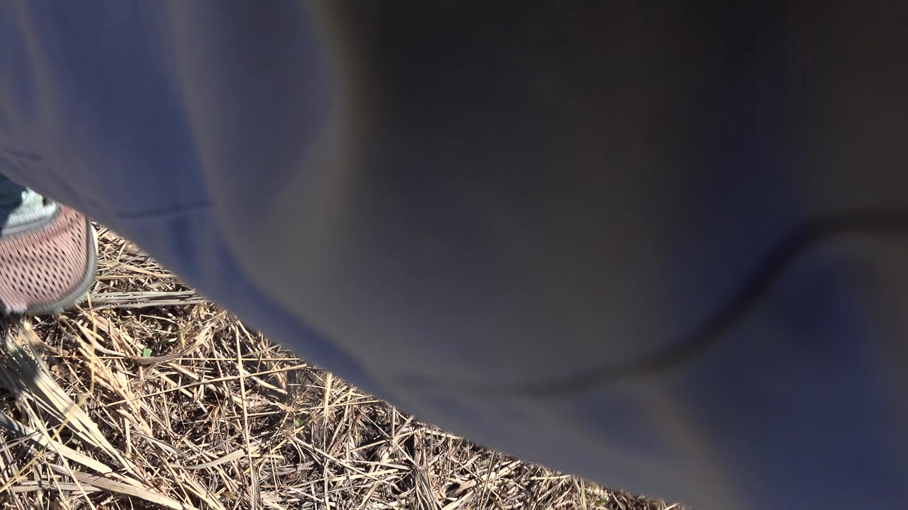 Close Mesa, Colorado trail frame with dark pants dominating the foreground, a shoe at the edge, and dry grass below in harsh sunlight.