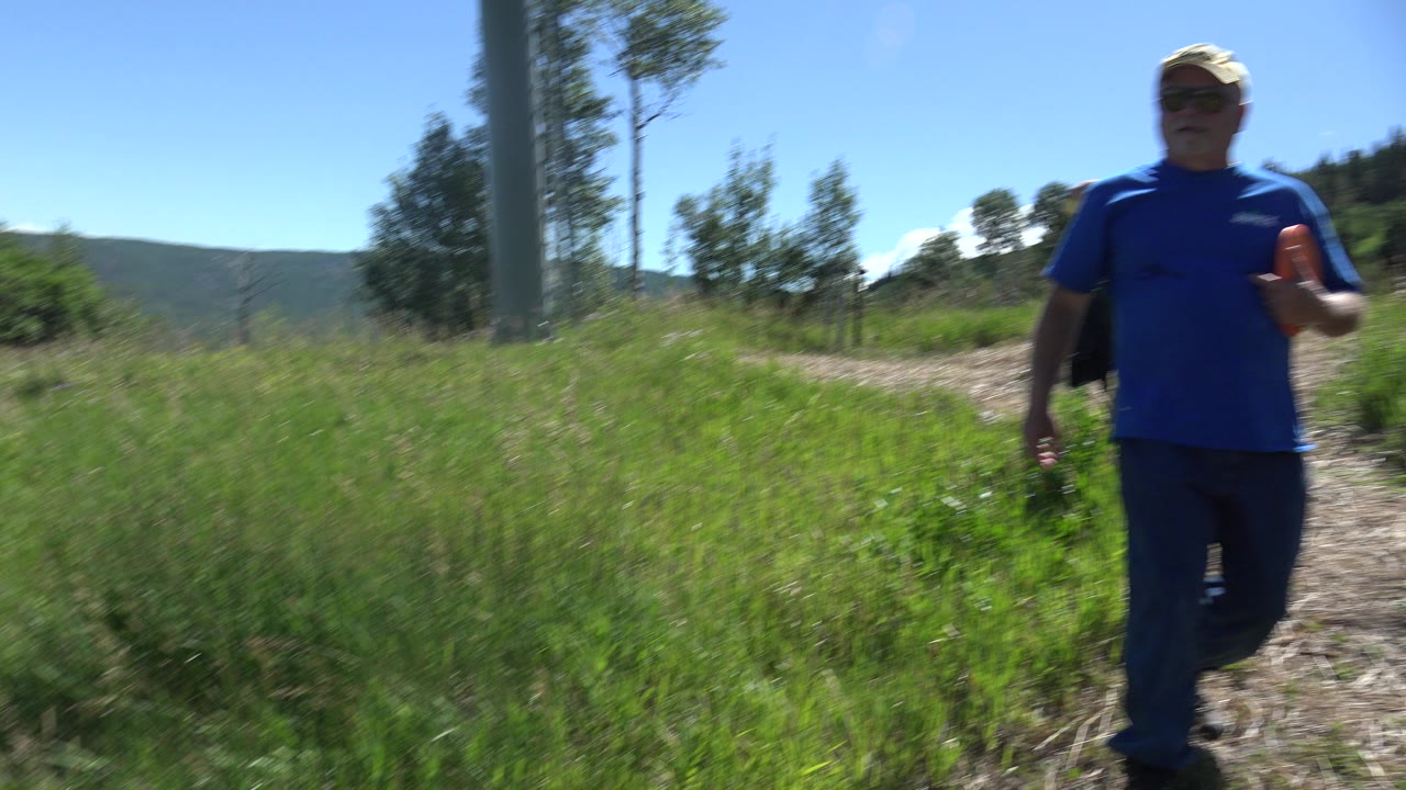 Man in blue shirt walking on a grassy dirt trail
