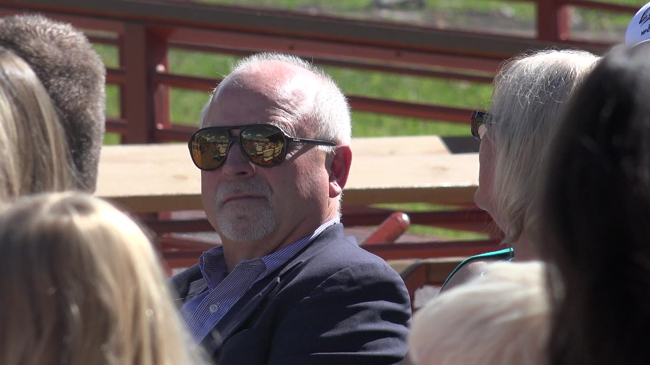 Man in sunglasses seated among outdoor spectators.