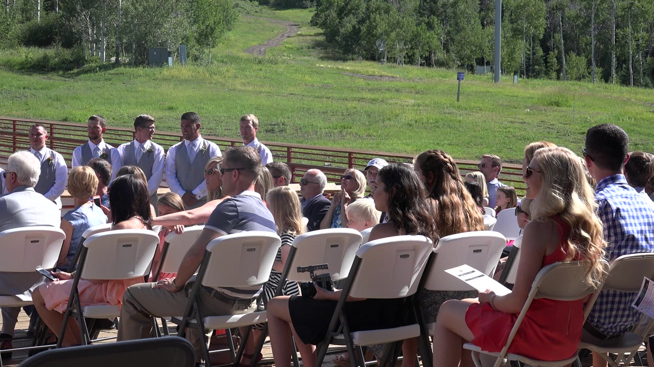 Outdoor wedding guests seated in folding chairs facing attendants.