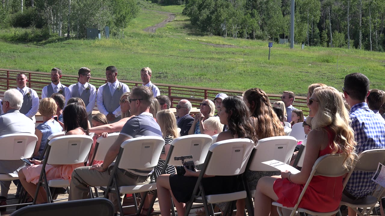 A similar Mesa, Colorado ceremony view shows guests seated in white folding chairs while men in light shirts and vests stand in front of the group.