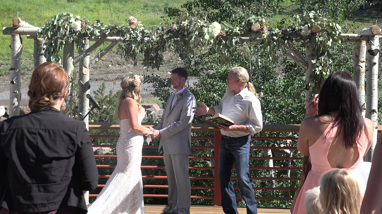Outdoor wedding ceremony with bride, groom, officiant, and guests.