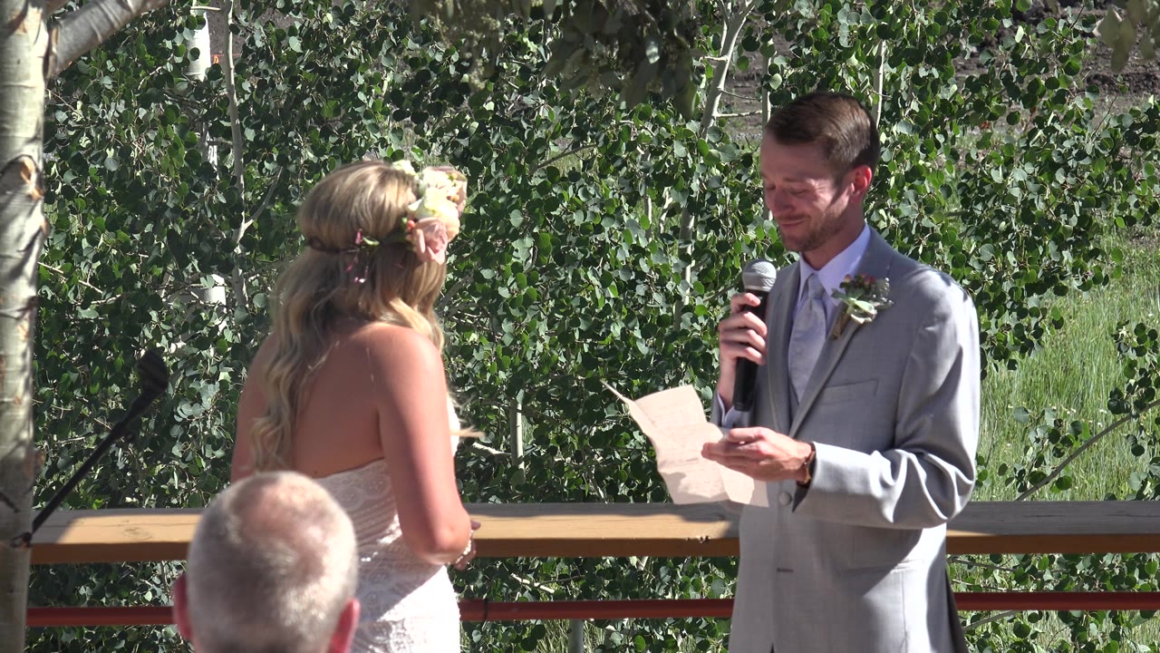 Groom reads from paper to bride during outdoor wedding ceremony.