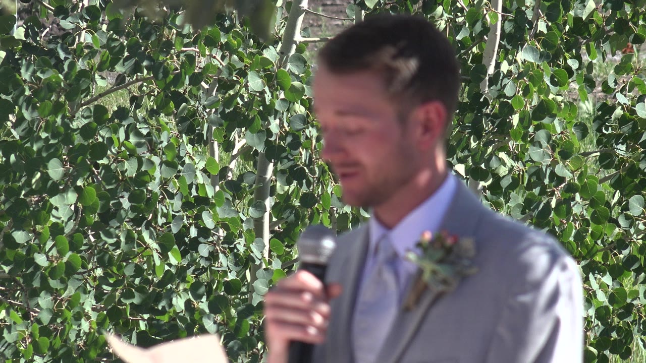 The groom remains softly focused while holding the microphone near his mouth against a dense leafy backdrop in Mesa, Colorado.