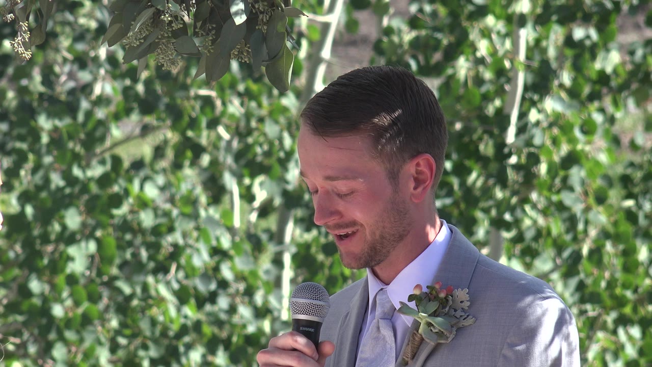 Man in grey suit holding a microphone outdoors