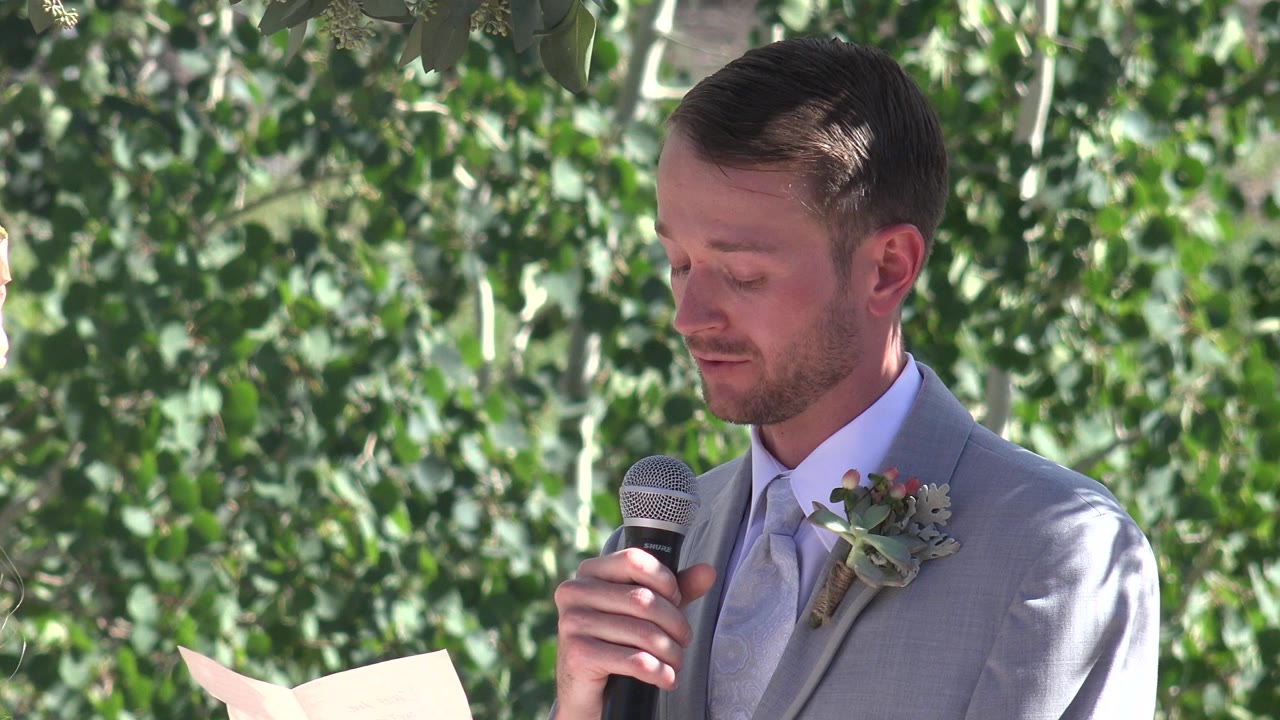 One second in, the Mesa, Colorado wedding speaker remains in profile-facing view, eyes lowered to his notes, with leaves filling the background.