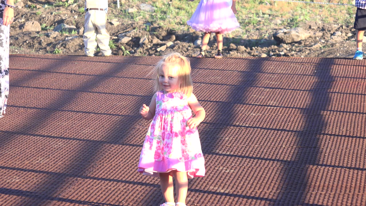 Young girl in a pink dress walking on a dark red deck.