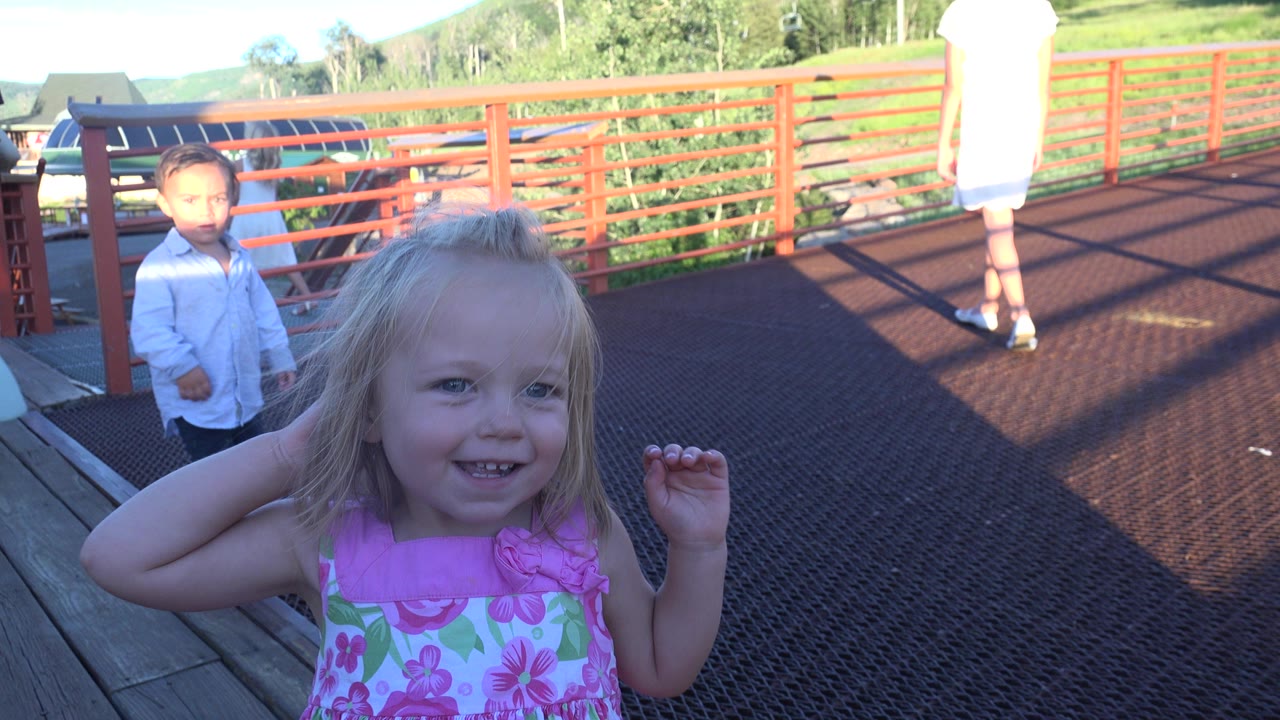 Young girl smiling on a red bridge with a boy behind her.