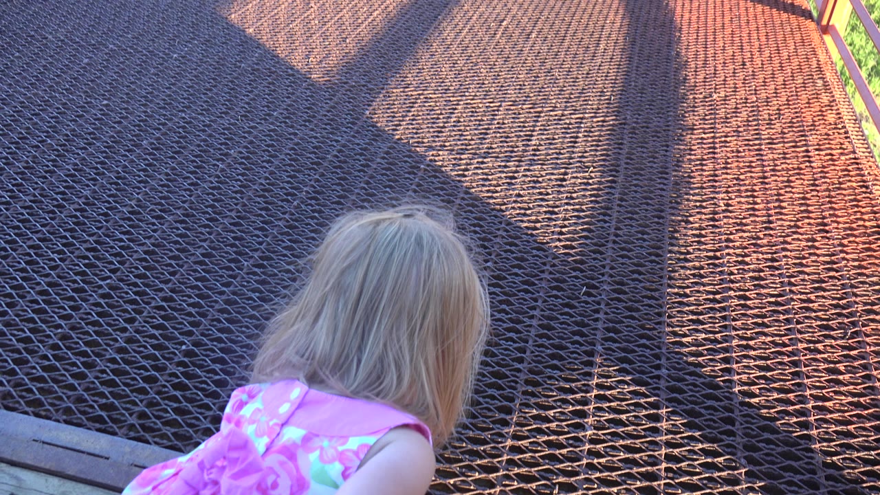 Young blonde girl in a pink dress bends near a metal grate.