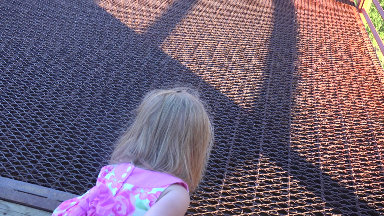 At 0:01 in Mesa, Colorado, the girl remains bent over with her head lowered toward the deck edge and metal grate catching warm light.
