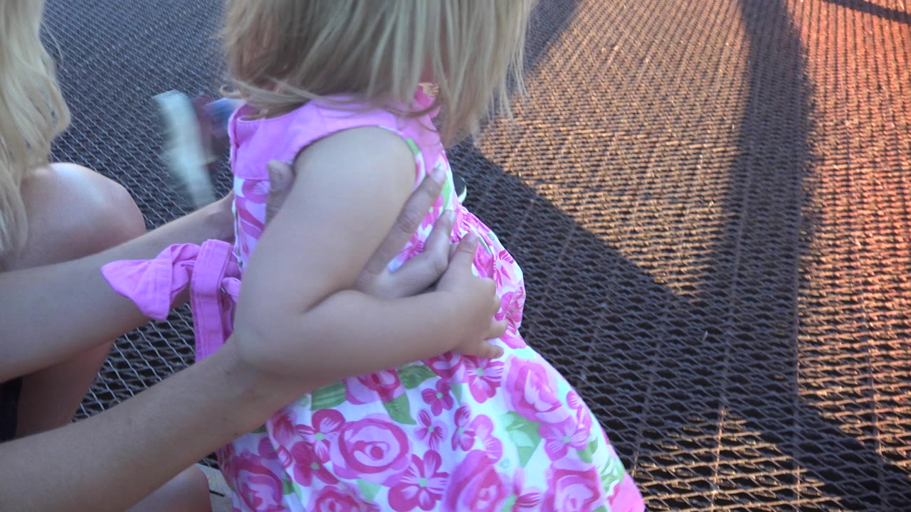 Young child in a pink floral dress held on a metal mesh walkway.