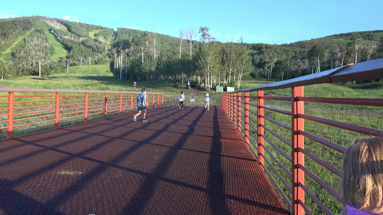Children running along a red metal walkway toward trees and a hillside.
