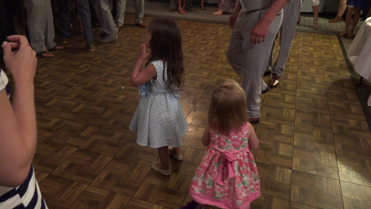 Two young girls stand near adults on a parquet dance floor.