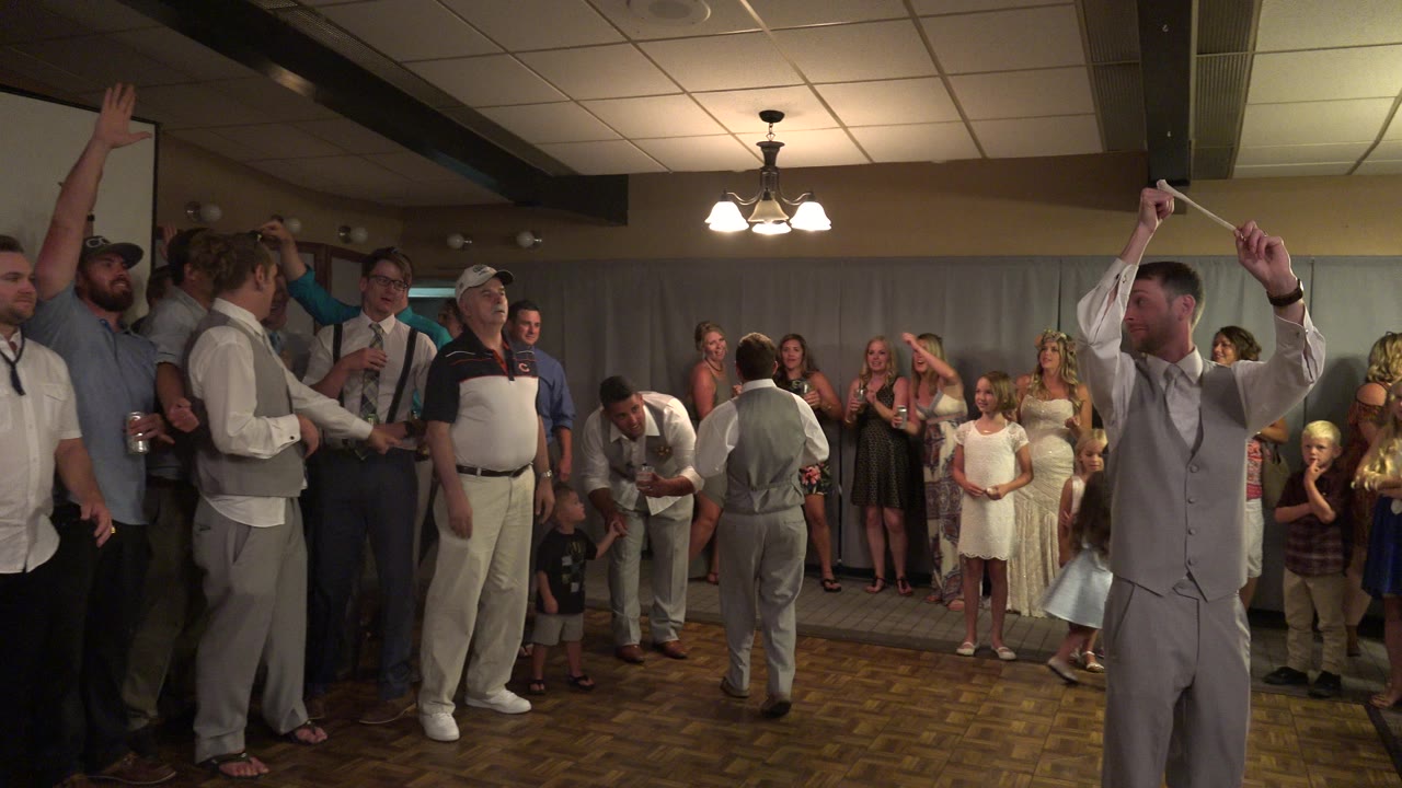 At 0:00 in Mesa, Colorado, wedding guests stand around an indoor dance floor while a man in a gray vest raises both arms in the foreground.