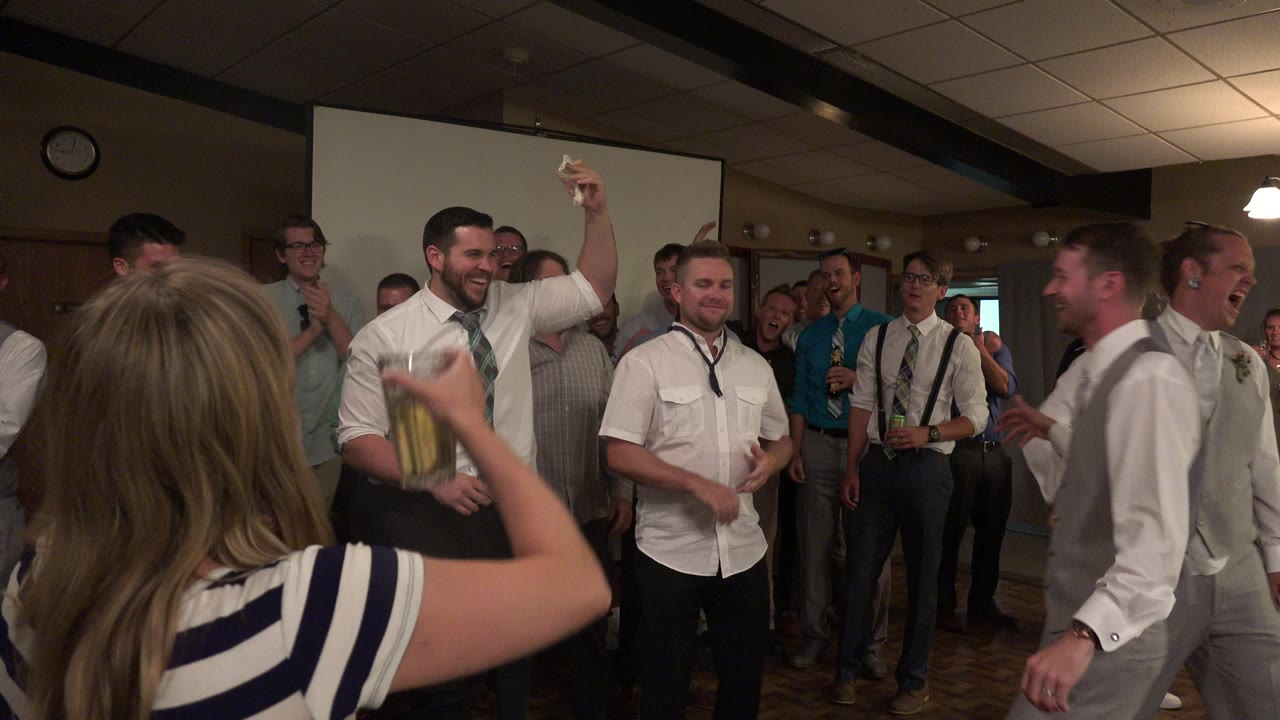 Adults gathered in a dim party room around men in white shirts.