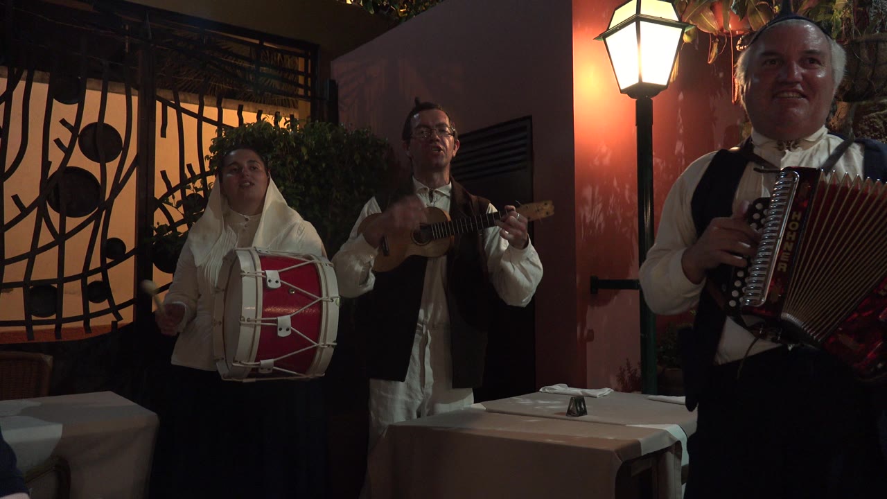 The accordion player stands closest to the lens while the drummer and guitarist remain visible in the background of the Madeira indoor music performance.
