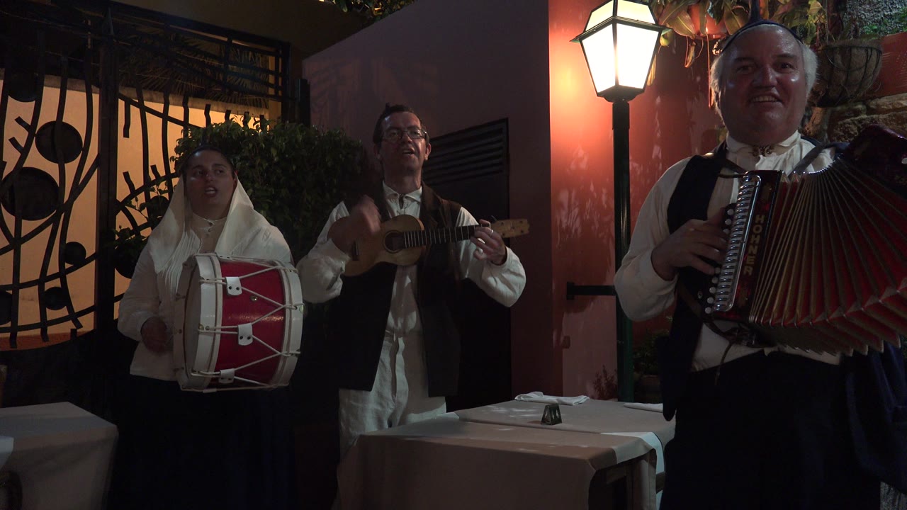 Three musicians performing beside a restaurant table at night.