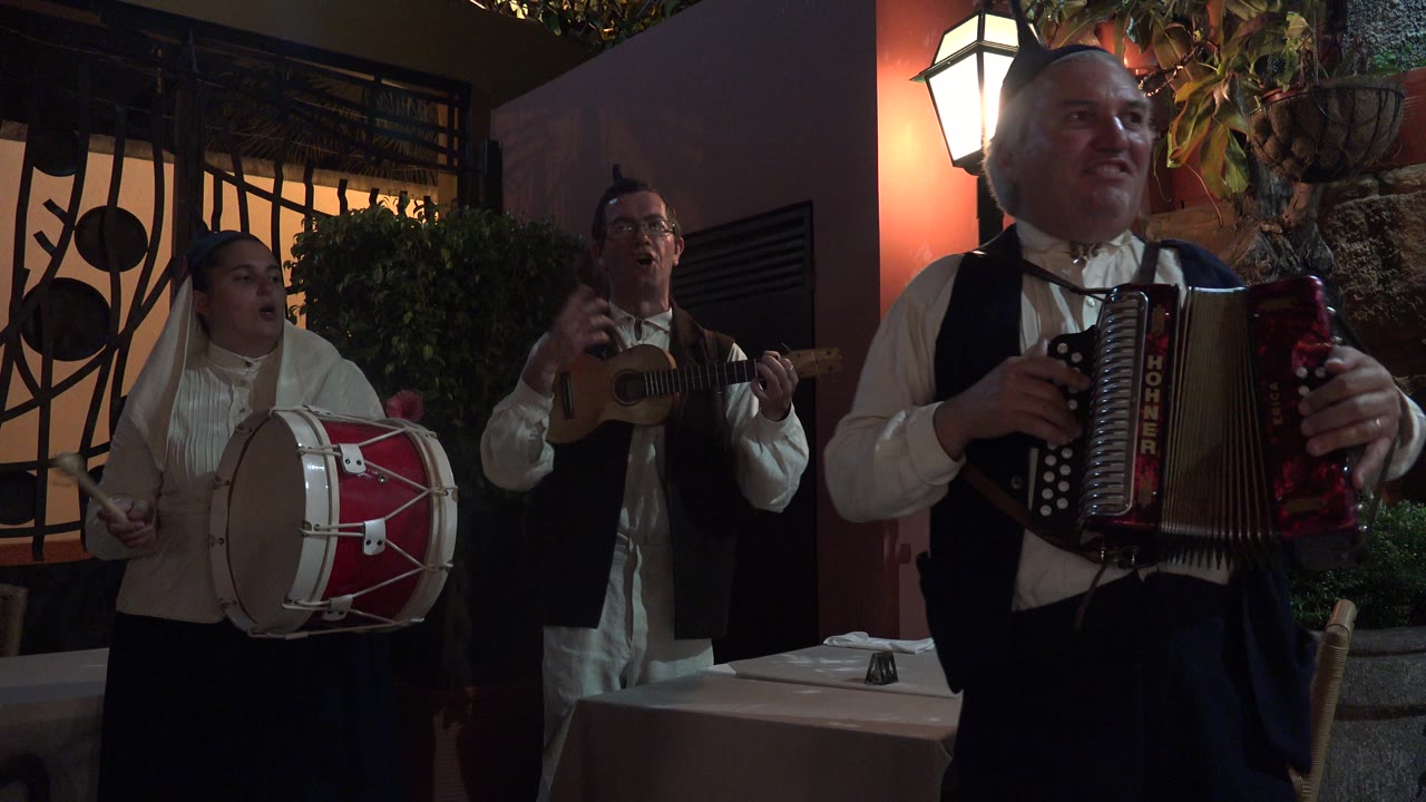 In Madeira, Portugal, the drummer and string player sing in the background while the accordion player fills the right side of the frame beside a glowing wall lantern.