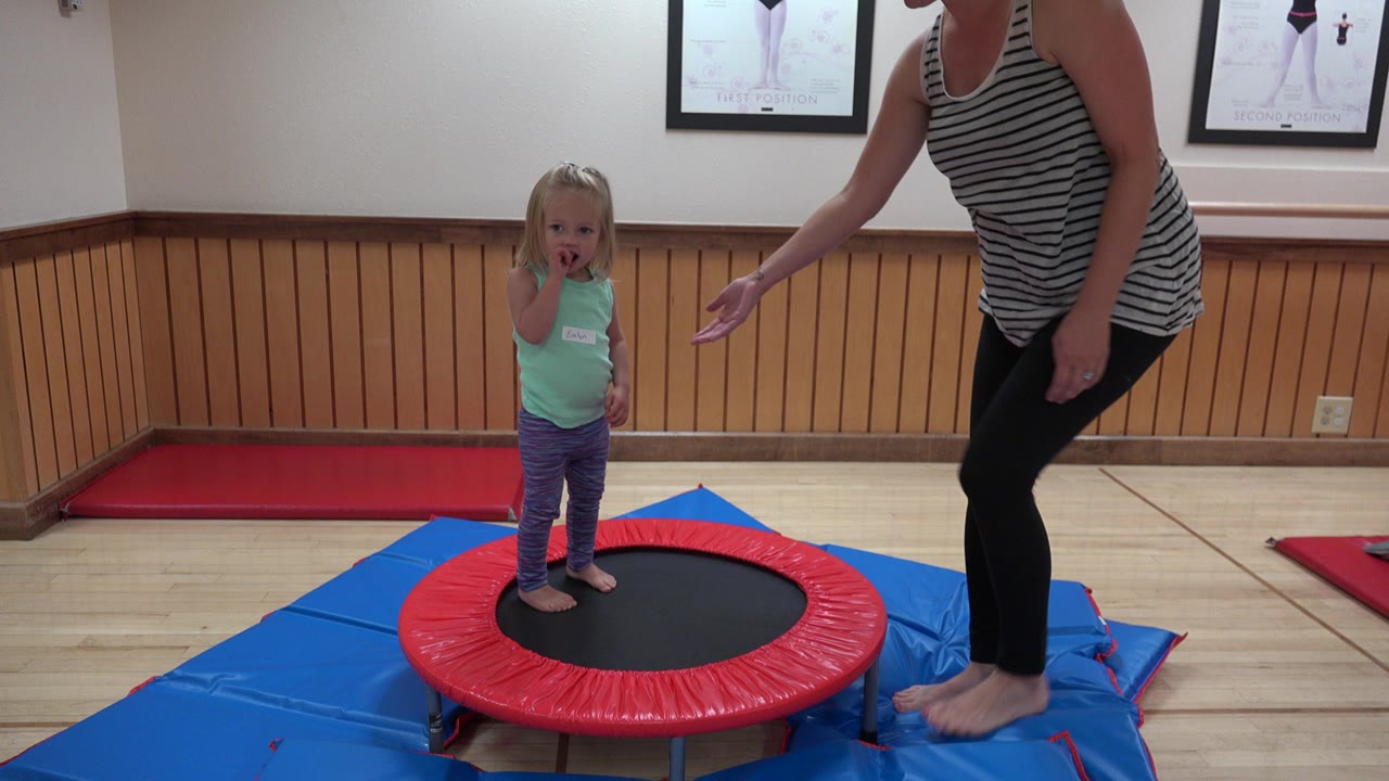 Young blonde girl on a red mini trampoline beside an adult woman.