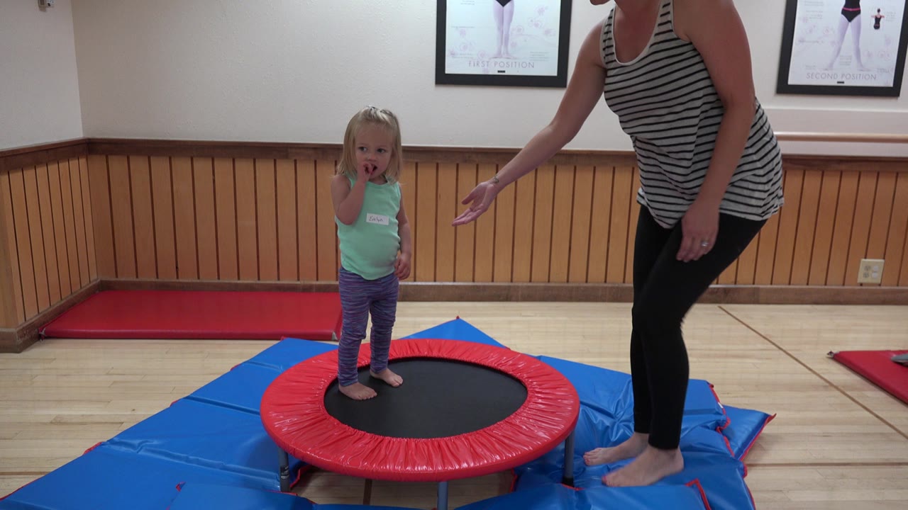 At 0:01 in Westminster, Colorado, the child remains centered on the trampoline as the adult woman leans in from the right with her hand extended.