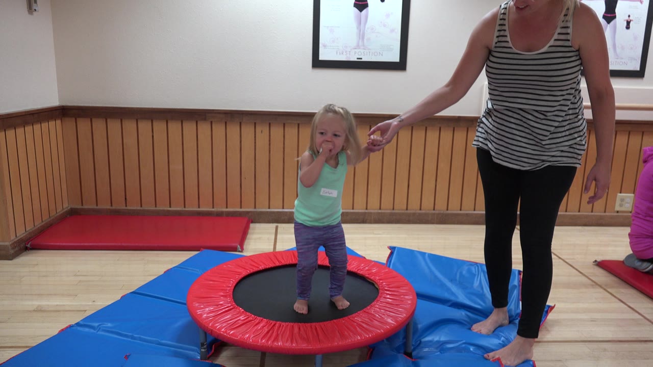 Child standing on a red mini trampoline next to an adult woman.
