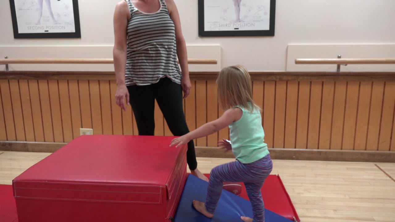 Young girl reaches toward a red padded block while her mother stands nearby.