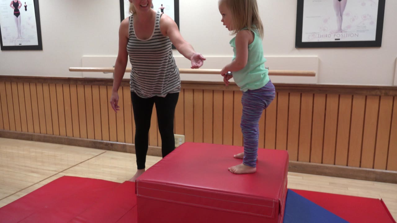 Woman holding a child's hand beside a red gym block.