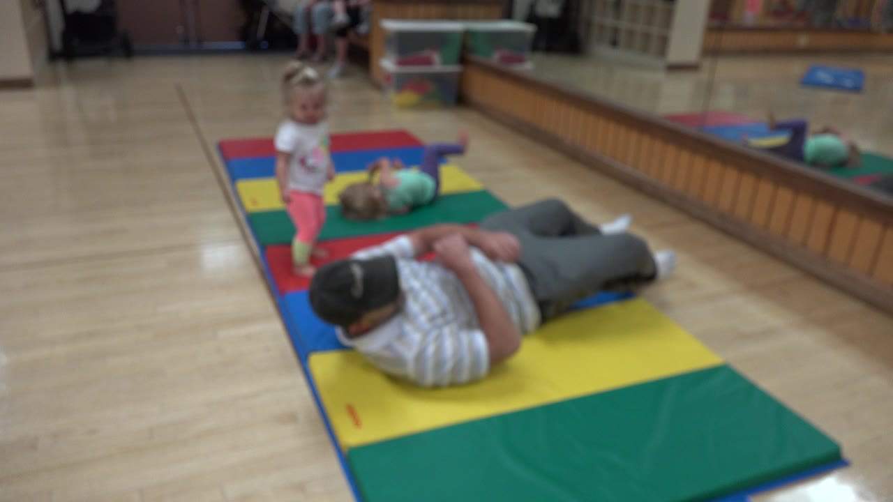 Father lying on a colorful mat with a toddler standing nearby.