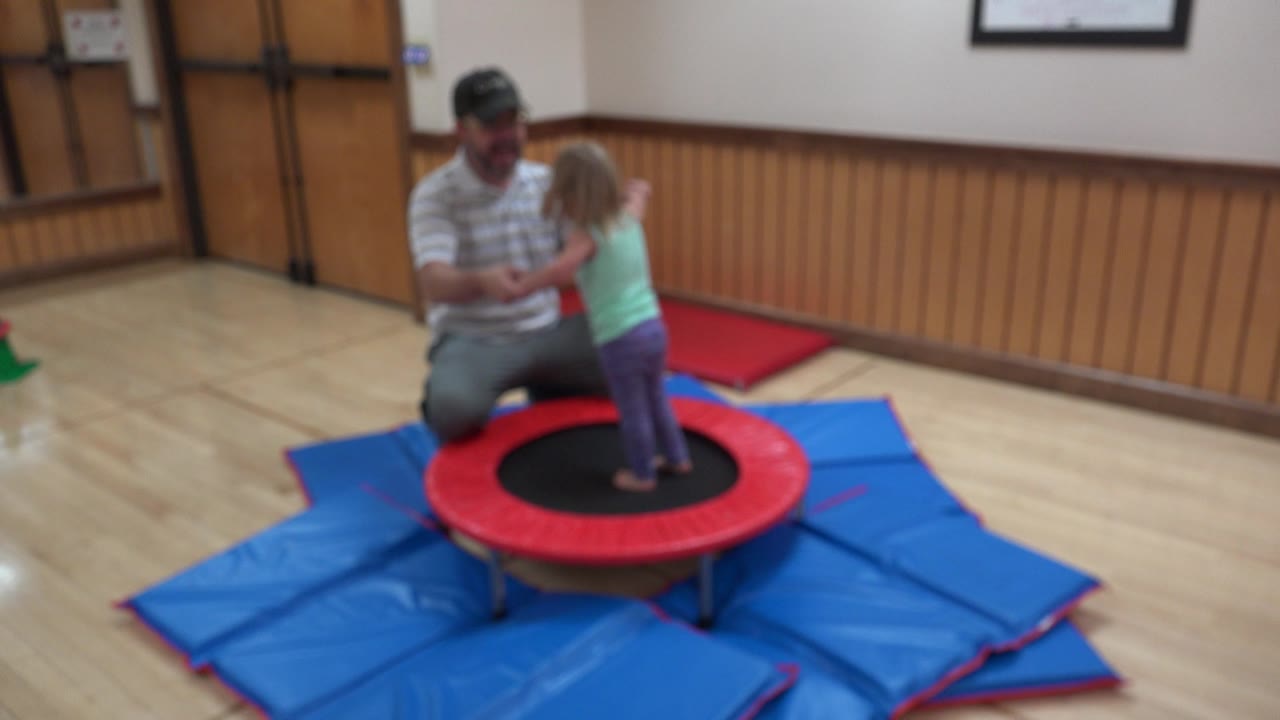 The young girl faces the kneeling man while he holds her hands on the indoor trampoline in Westminster, Colorado.
