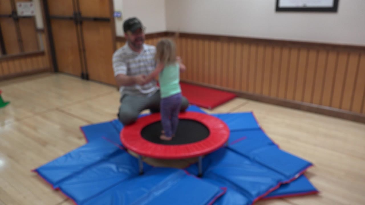 Child balancing on a trampoline with a man beside her.