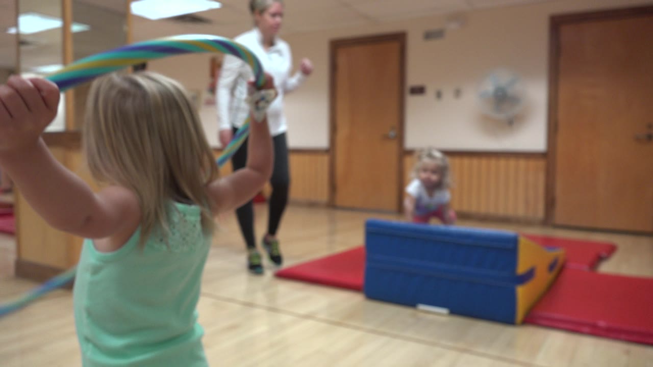 Child raises both arms with striped ribbons in a gym studio.