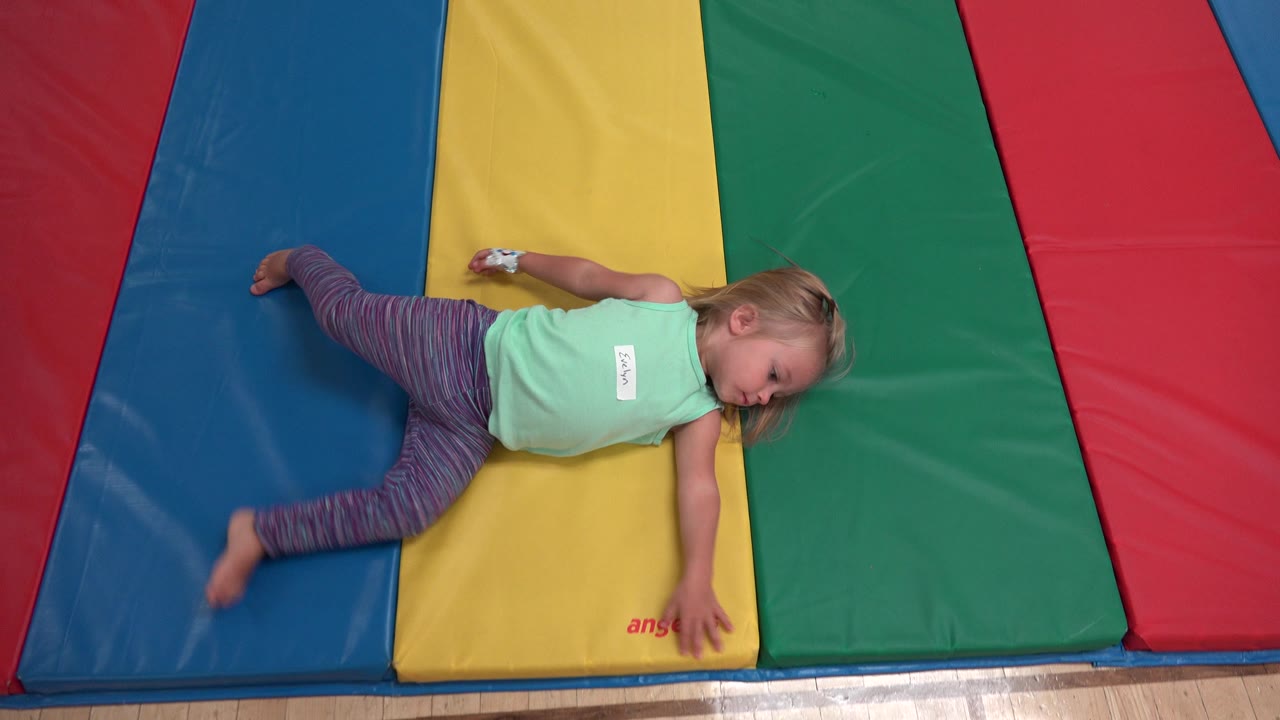 Girl sprawled across padded mats near wood floor.