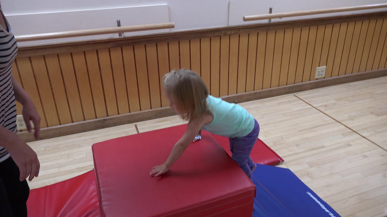 In Westminster, Colorado, the child has moved farther onto the red padded block, with one hand planted near the center and the adult still partly in frame.