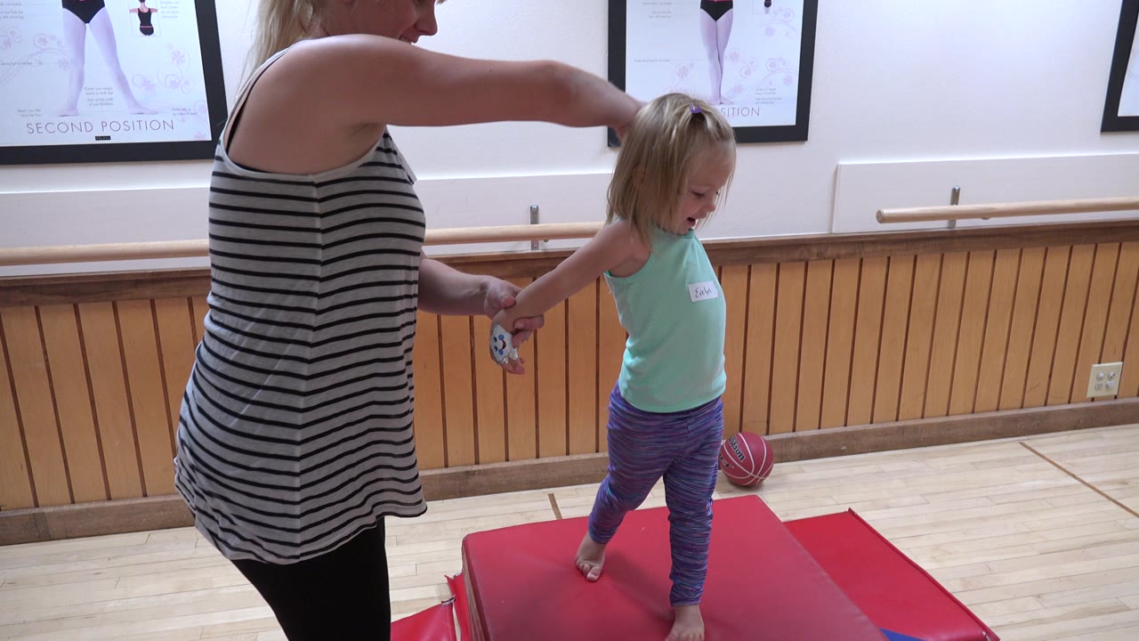 Woman guides a child stepping off a red mat in the gym room.