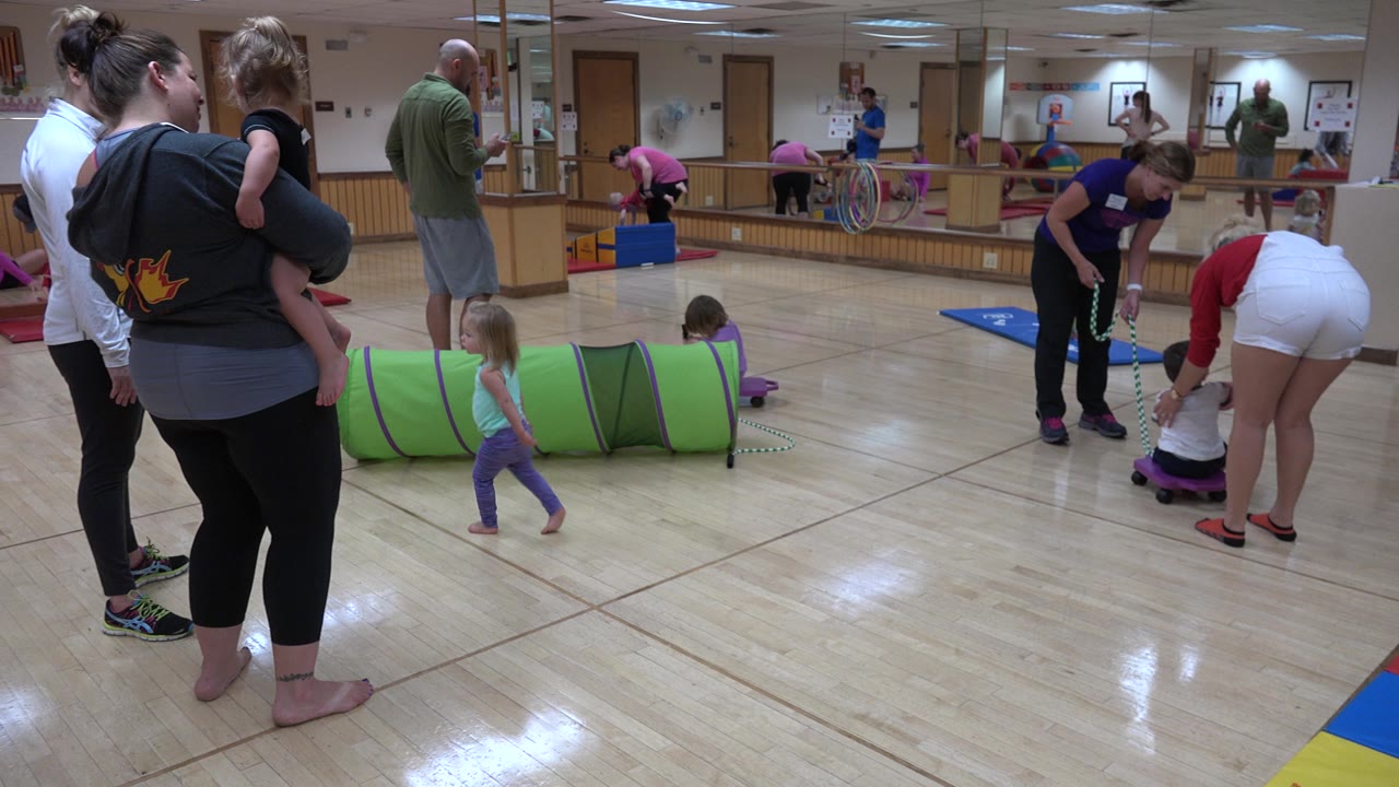 Woman holding a child while other children play near mats and toys.