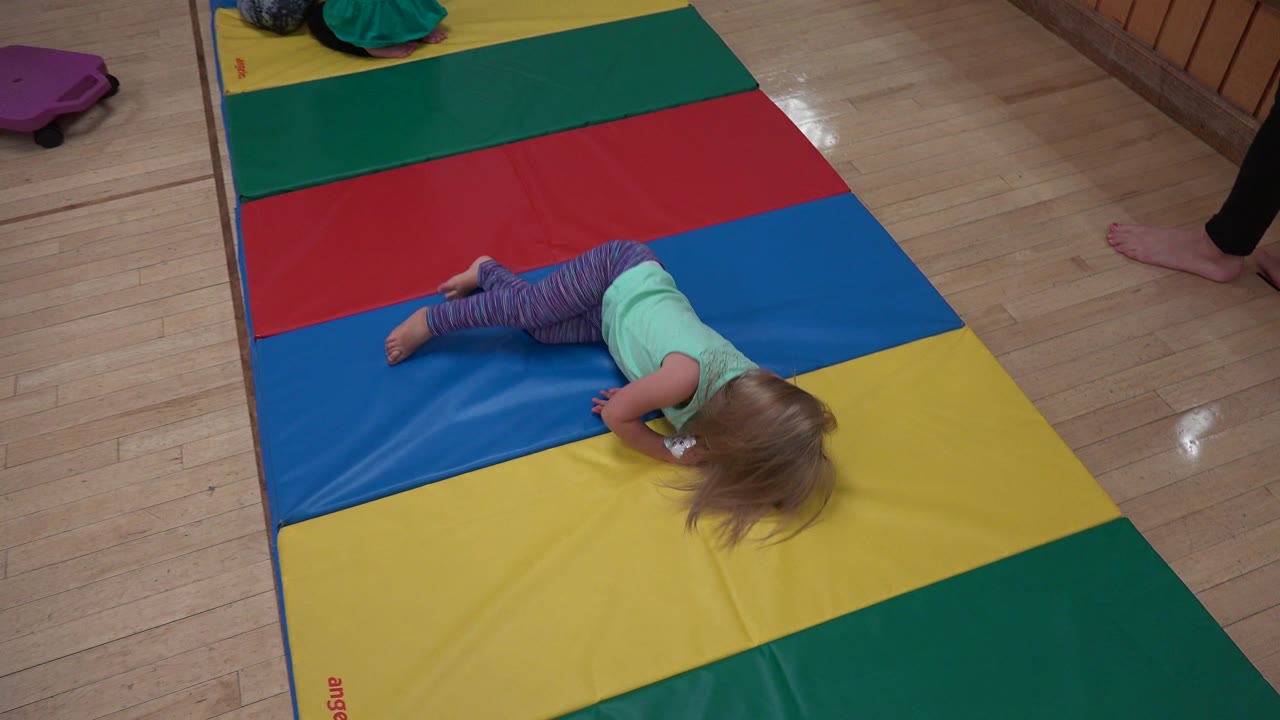 Child lying face down on a colorful padded mat.