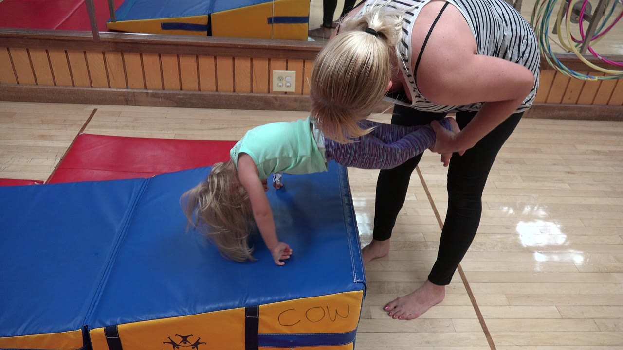 Woman holding a young child upside down over a blue play mat.