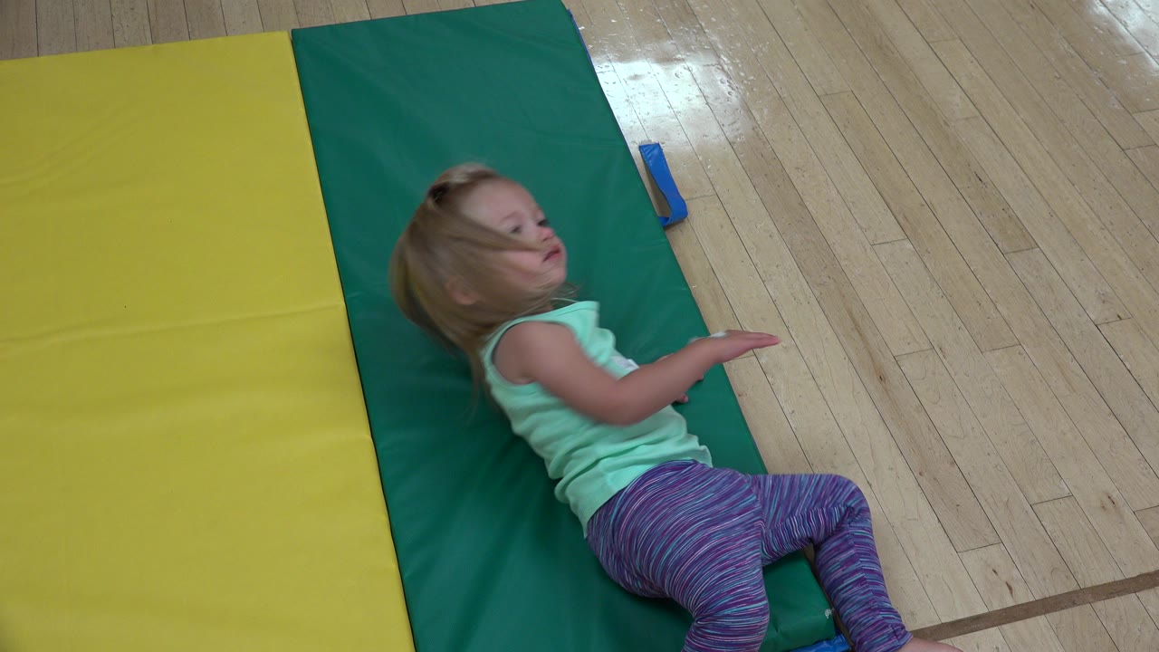 Young blonde girl in a mint top and purple striped leggings lies partly on a green mat beside a yellow mat in Westminster, Colorado.