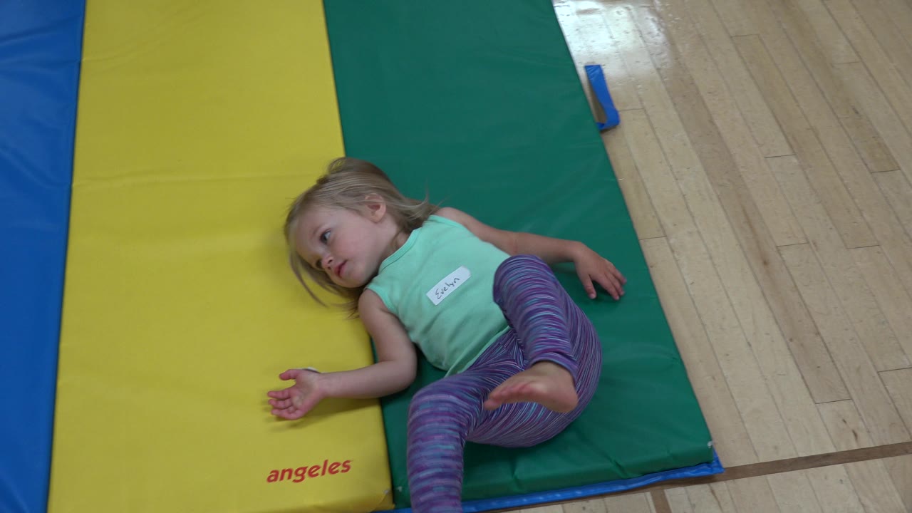 Girl lying across yellow and green mats looking upward.