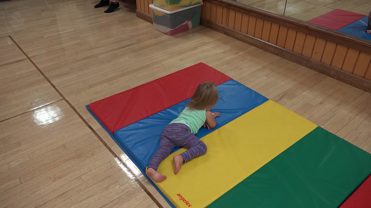At 0:00, a young girl in Westminster, Colorado crawls on a red, blue, yellow, and green padded play mat across a polished wood floor.