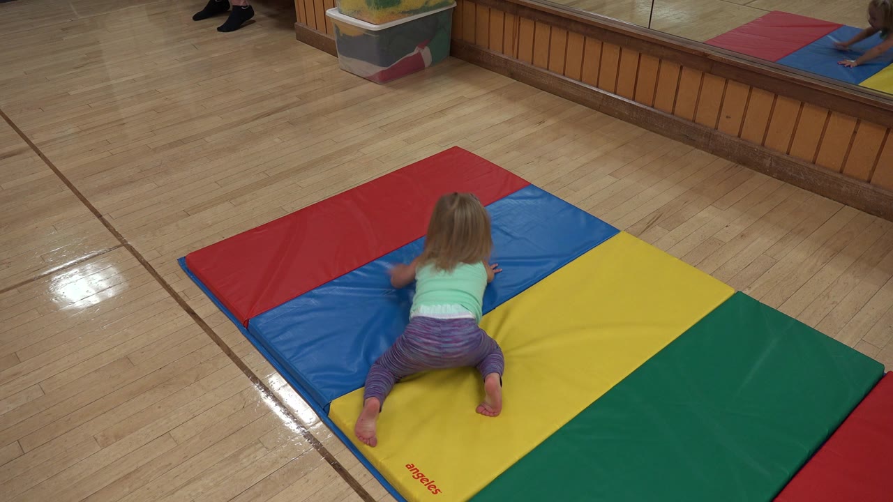 Young girl kneeling wide on a colorful play mat.