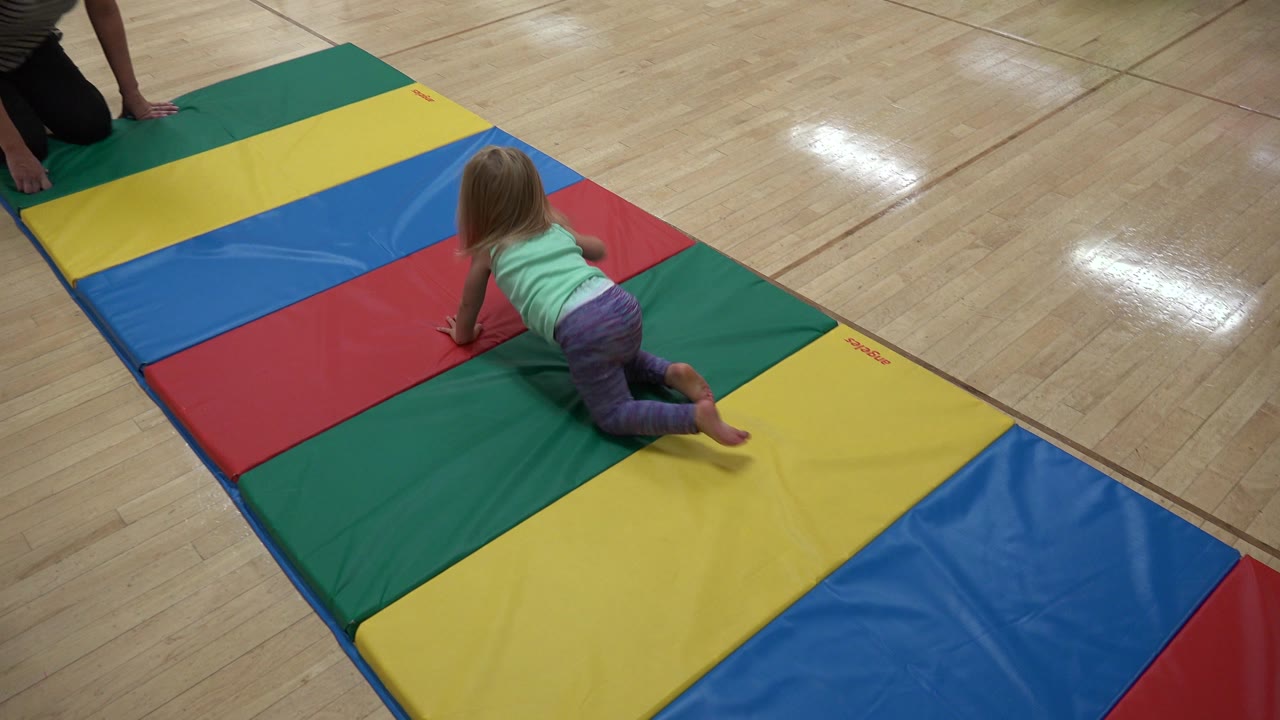 At 0:01 in Westminster, Colorado, the baby continues crawling down the padded mat while a kneeling adult remains partly cropped at the upper left.