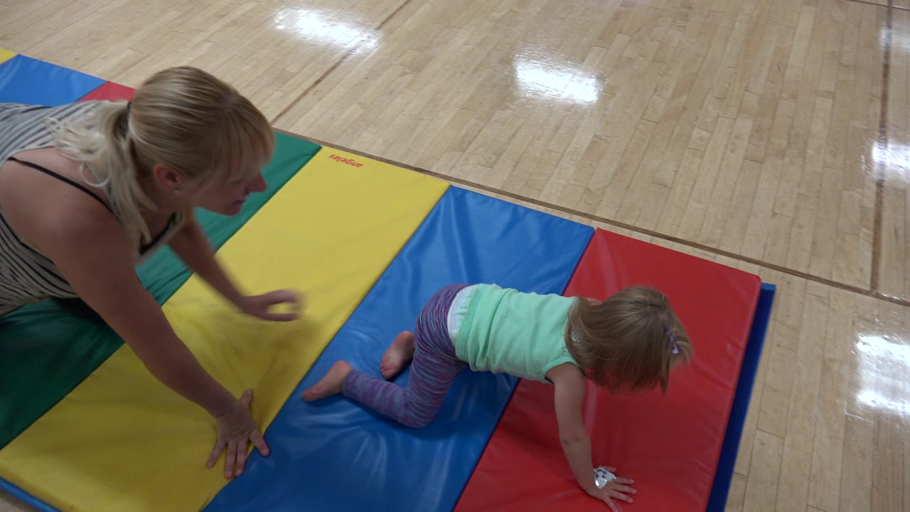 The young girl continues crawling across the blue and red sections of a padded mat as an adult woman reaches toward the yellow section in Westminster, Colorado.