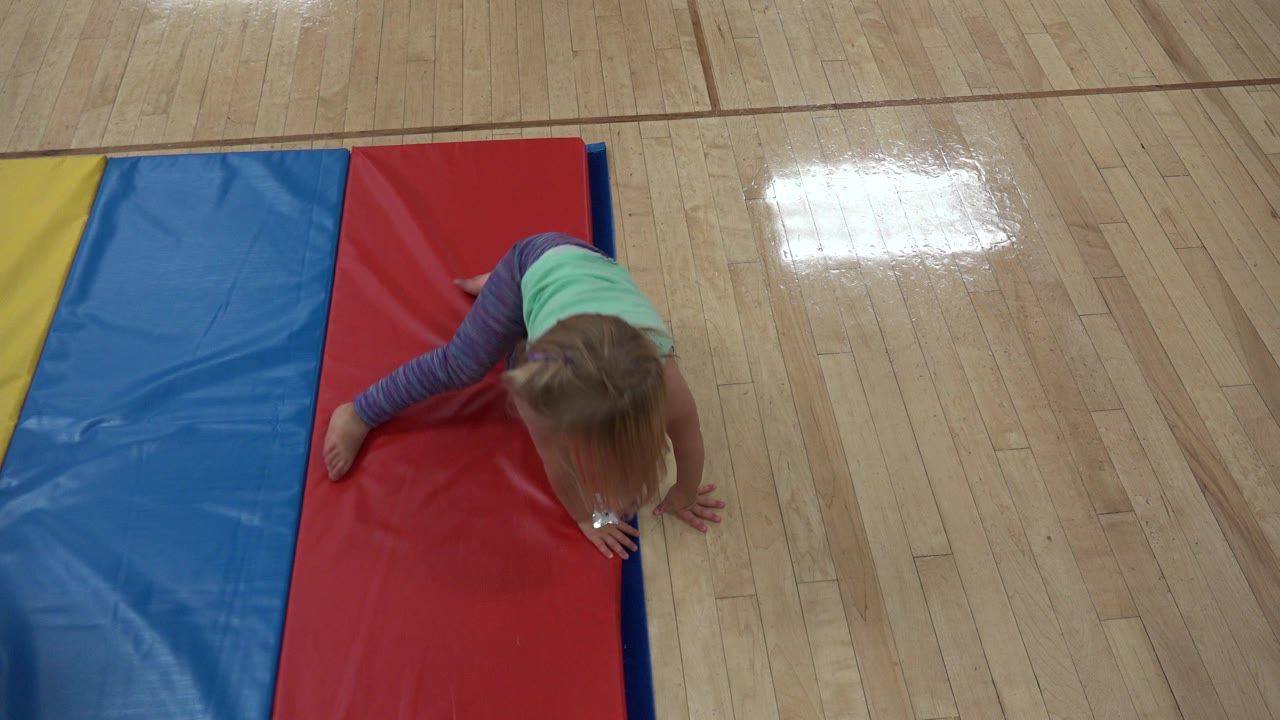 Young girl crawling on a red mat beside blue and yellow panels.