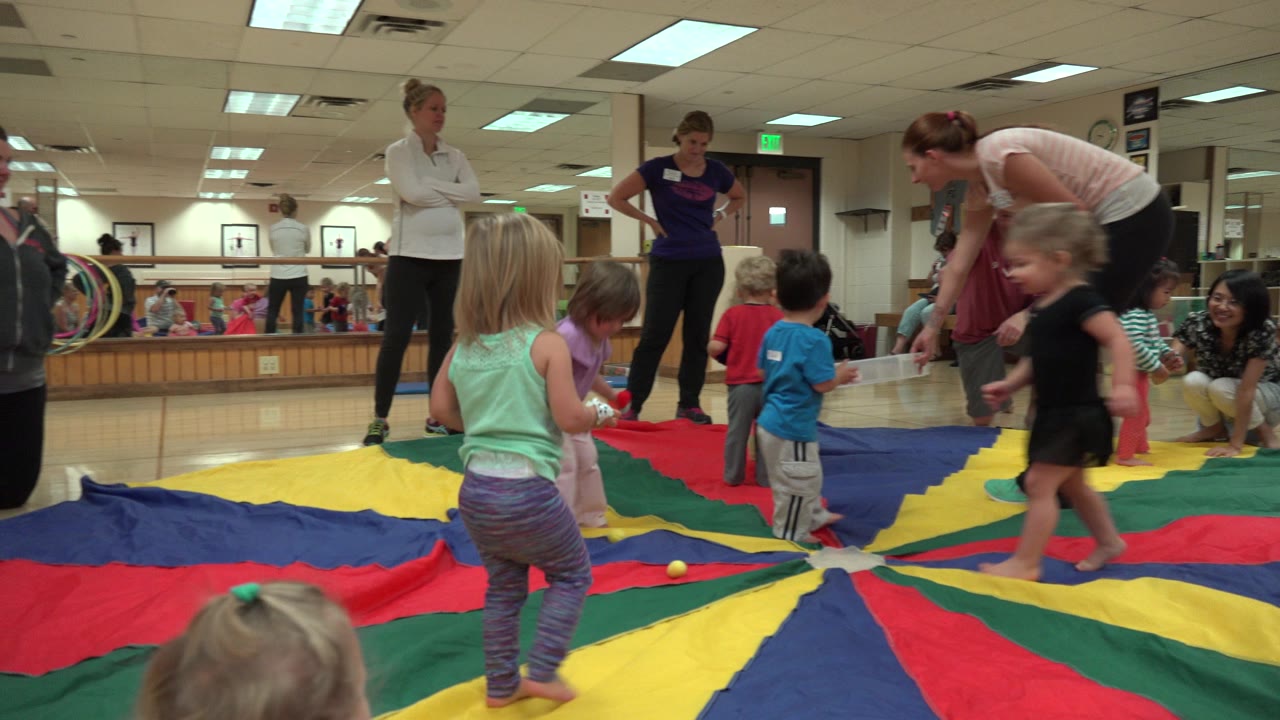 Toddlers and adults around a colorful gym play mat.