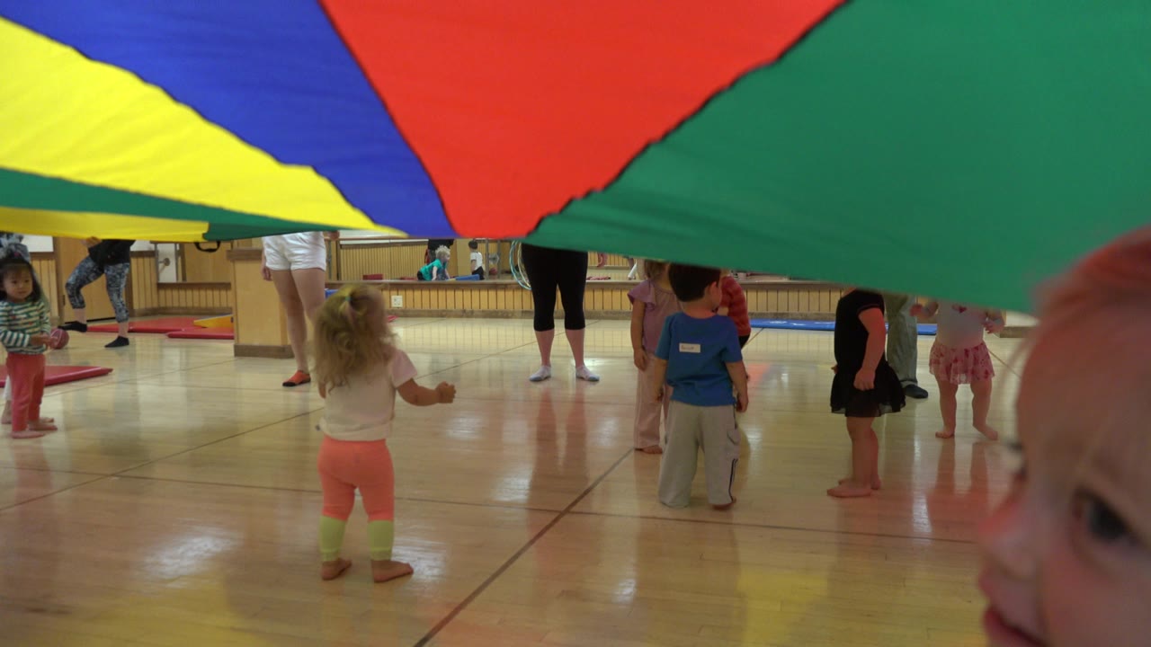 One second into the Westminster, Colorado footage, the colorful sheet still hangs low across the top of the frame while several children stand below it facing adult leaders.