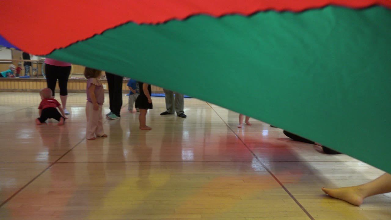 Large green and red parachute low over children on a polished floor