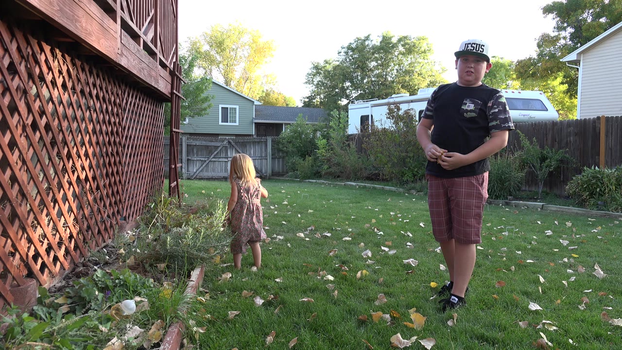 Two children in a fenced backyard beside a deck lattice.